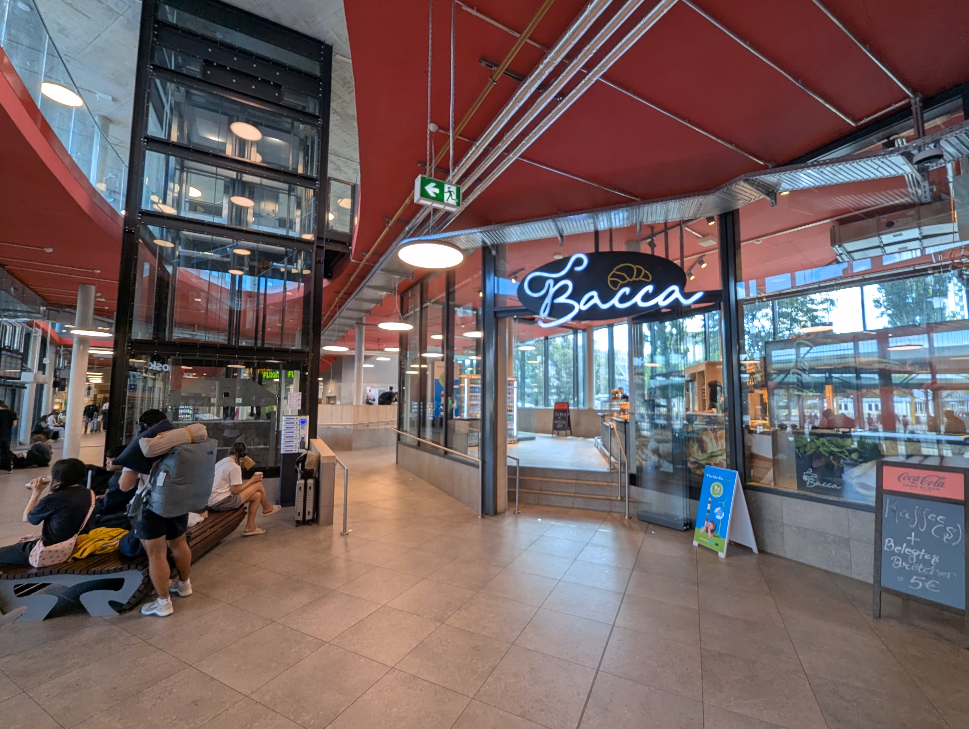 Ein Bild aus dem Zentrum der Wartehalle, im Zentrum befindet sich ein Aufzug, hinter welchem der Gastronomiebereich liegt.
